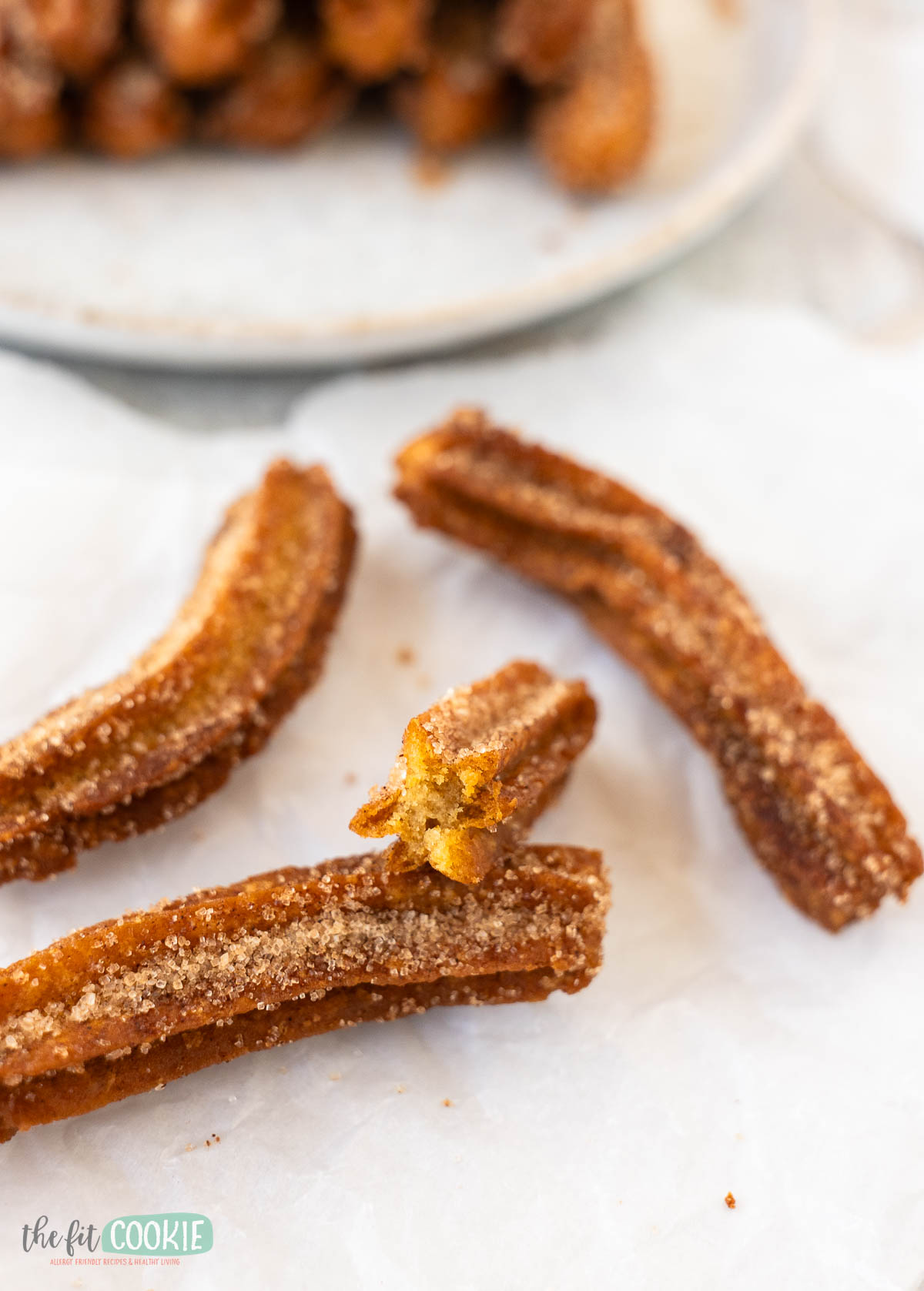 Three gluten free vegan churros coated in cinnamon sugar rest on parchment paper, with one churro cut in half to reveal its interior.