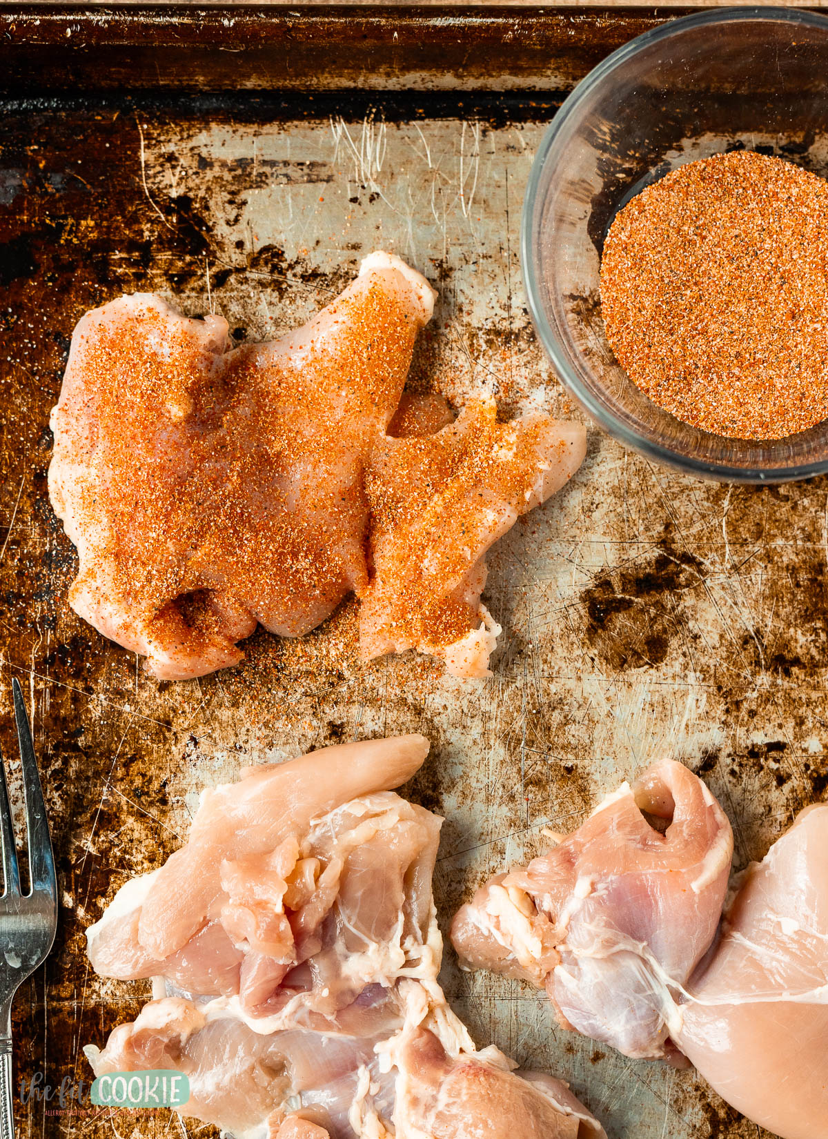 Raw chicken thigh pieces on a metal tray, some coated in spices.