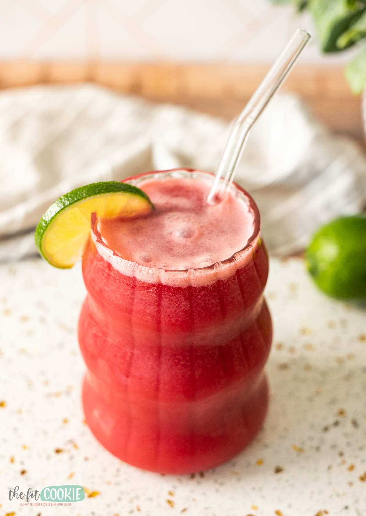 glass of dairy free brazilian cherry lemonade with a lime slice and glass straw. 