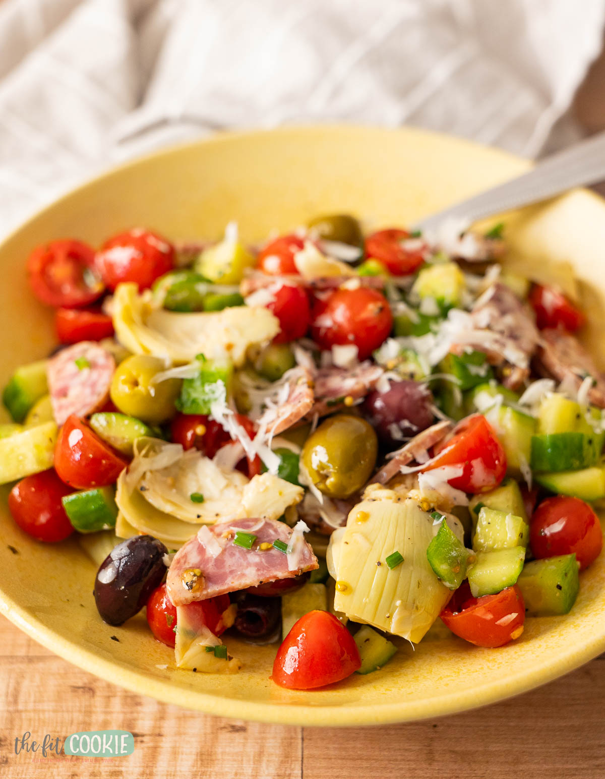 a close up photo of an italian chopped salad in a yellow bowl with dairy free parmesan on top. 