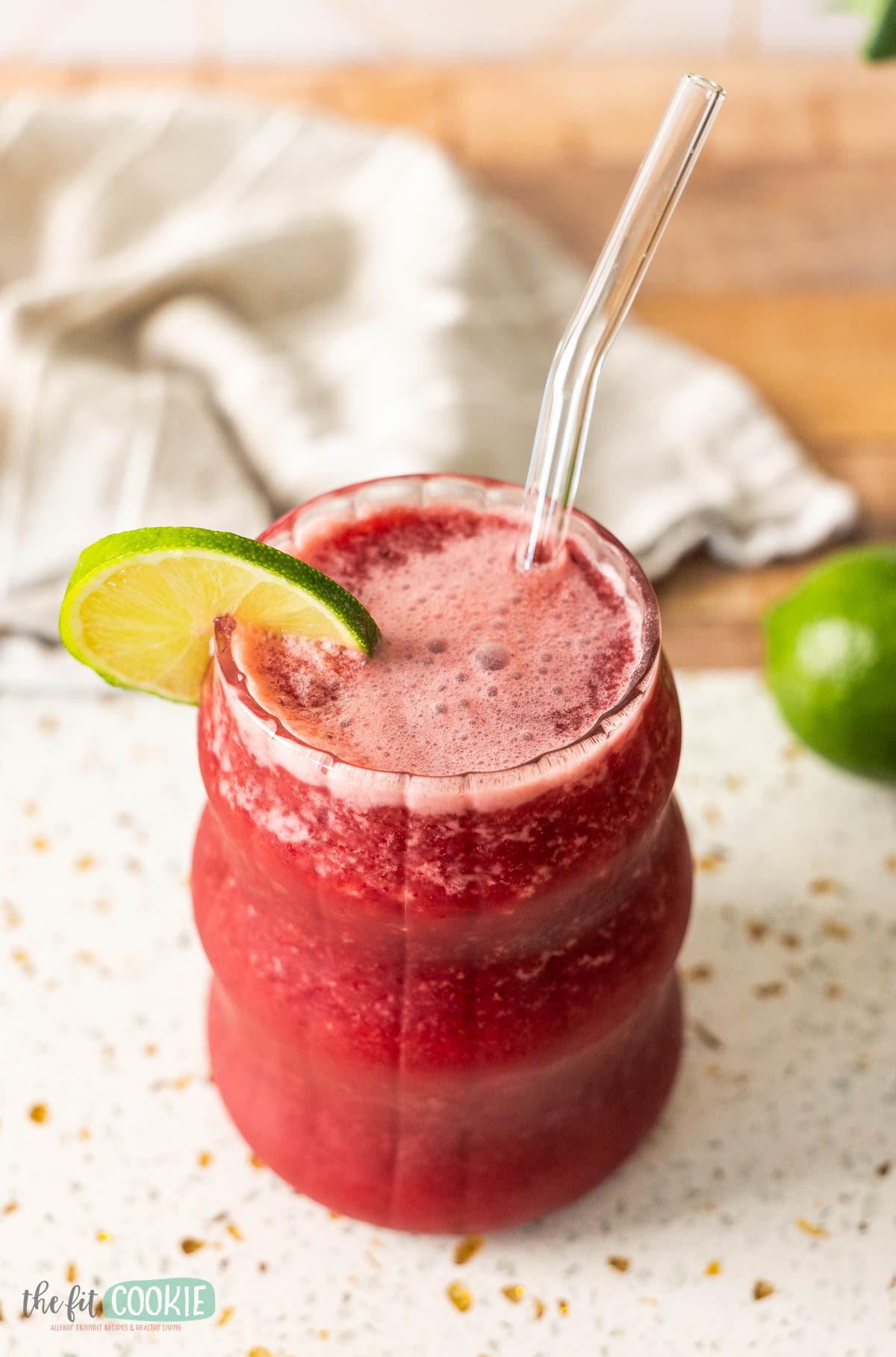 A red, dairy-free cherry brazilian lemonade in a wavy glass with a glass straw,.