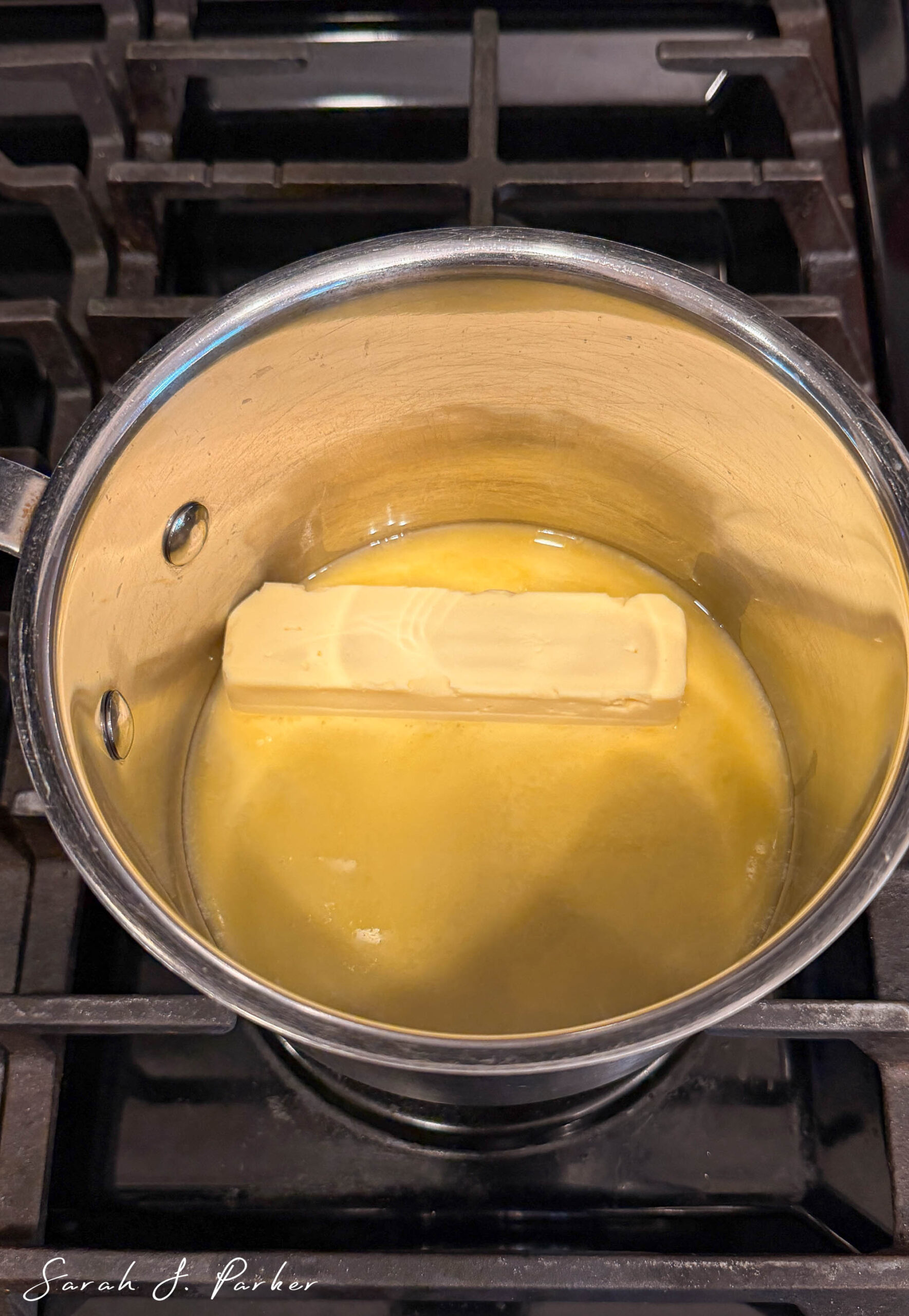 A stick of dairy free butter is partially melted in a saucepan on a stove burner.