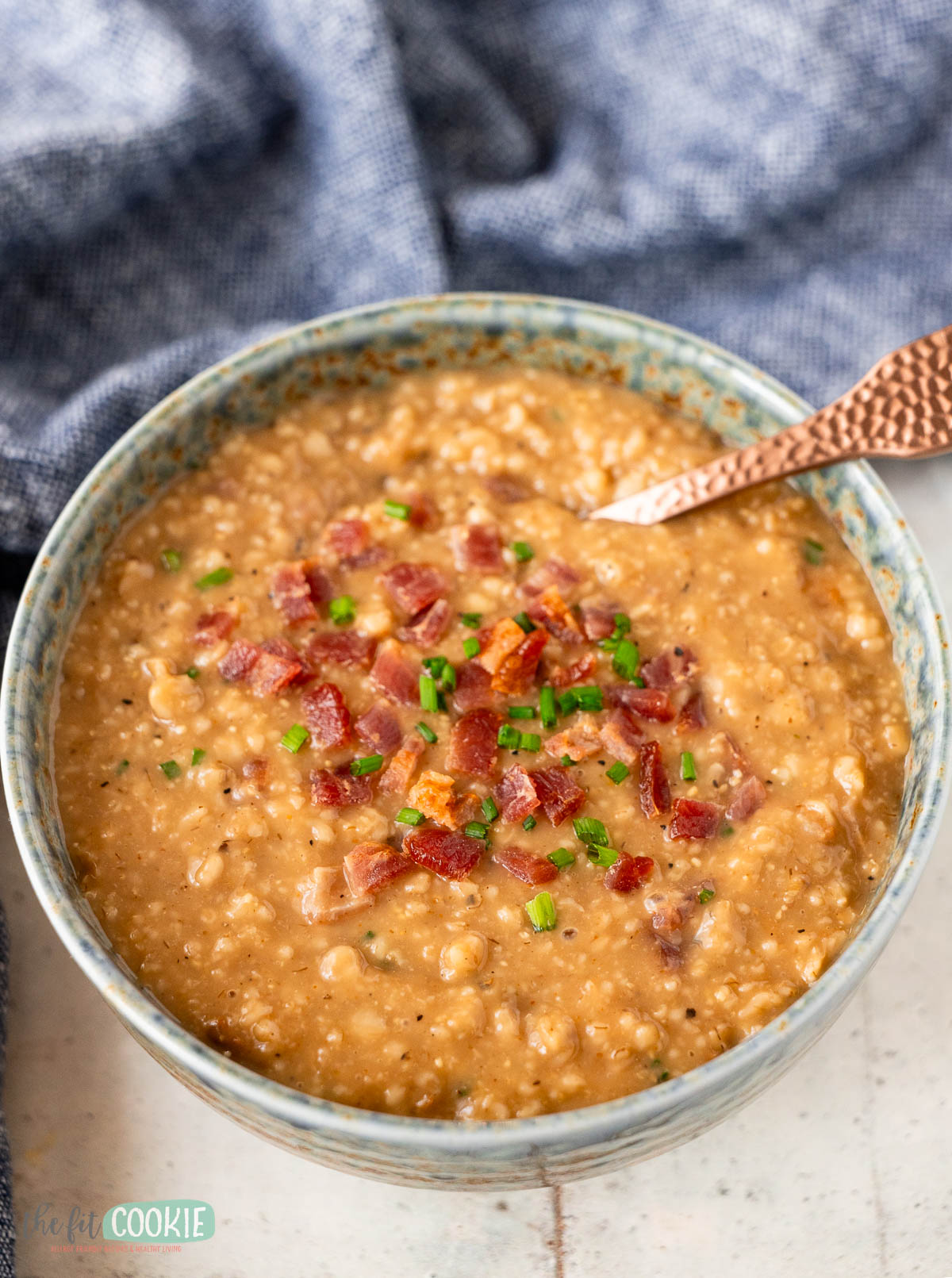speckled blue bowl filled with savory protein oatmeal and topped with bacon crumbles and chopped chives.
